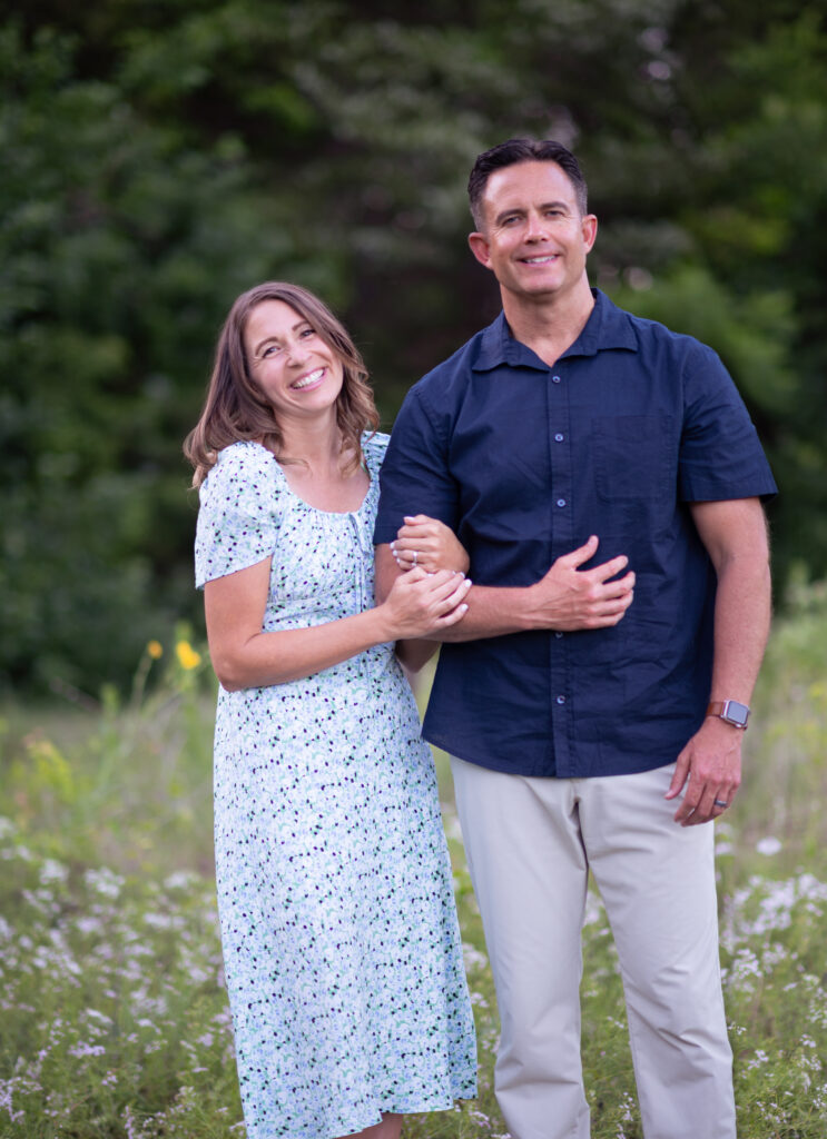 Michele Tripple smiling and linking arms with her husband while standing in a field of wildflowers.