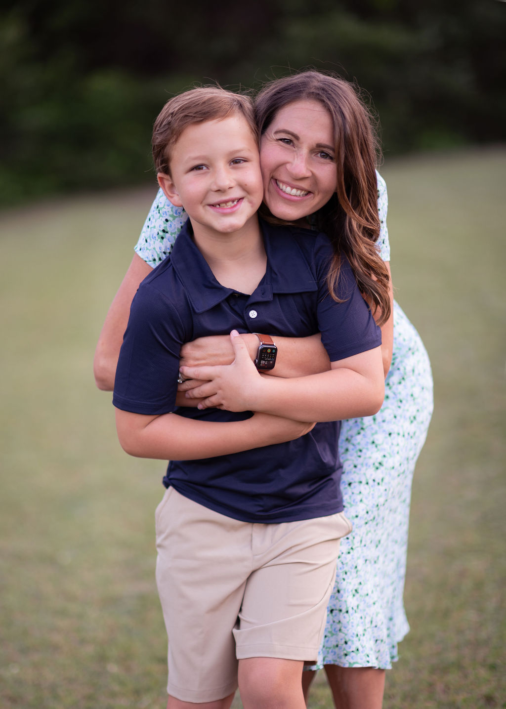 Michele Tripple hugging her smiling young son outdoors in a grassy field, both looking at the camera with joy.